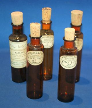 A Set Of Five Amber Glass Apothecary Bottles,  Paper Labels,  Cork Stoprs